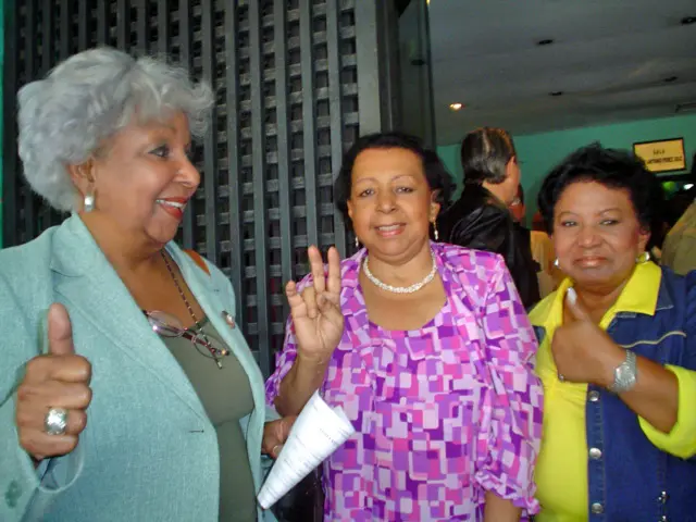 Three women celebrating and waving to the camera during an event